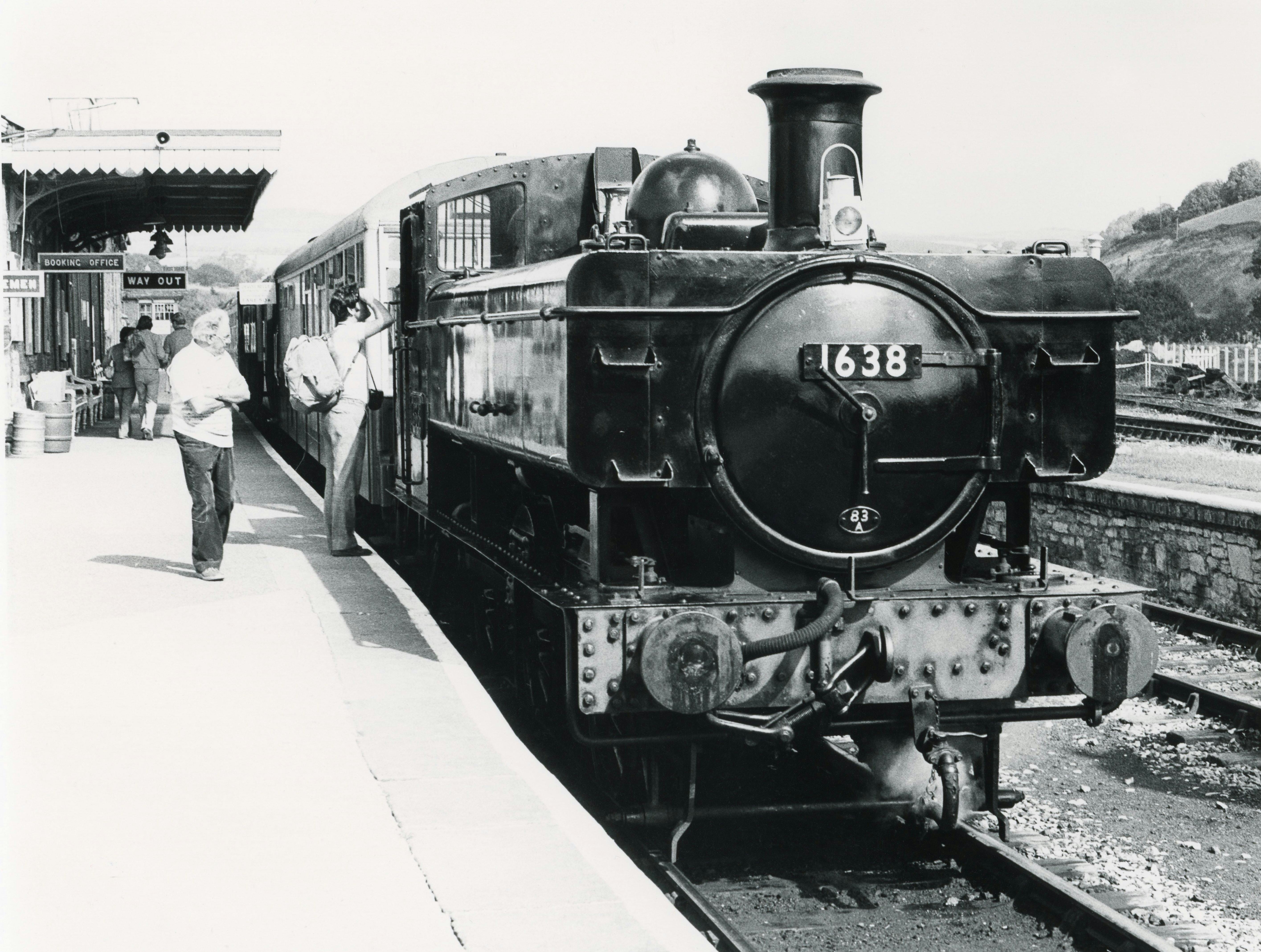 Classic black and white photo of a vintage steam locomotive at a bustling train station with passengers.