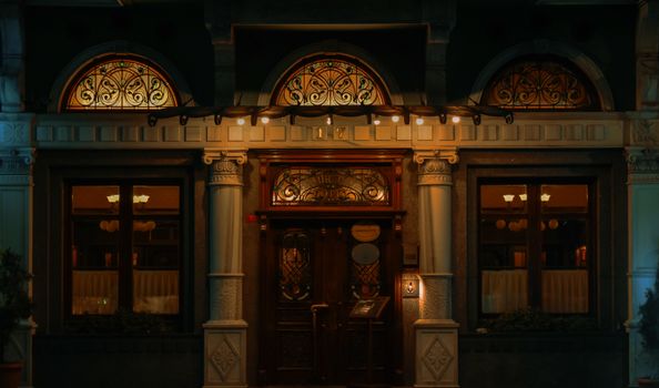 Charming evening view of a restaurant facade with ornate columns and intricate wooden doors.
