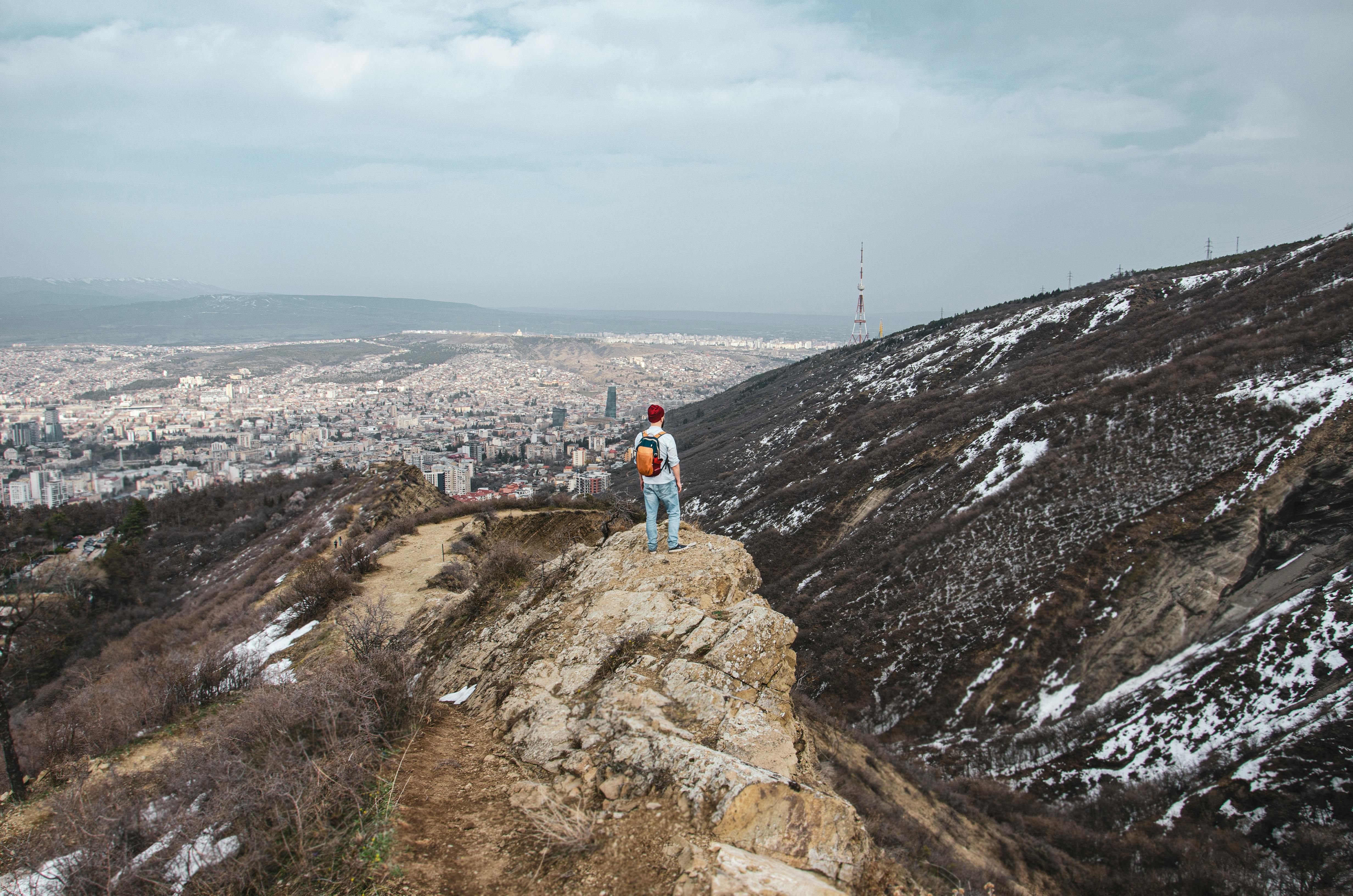 Prescription Goggle Inserts - A traveler stands on a snowy mountain edge with a panoramic view of Tbilisi cityscape.