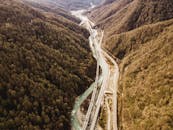 从空中俯瞰，一条风景秀丽的山区高速公路穿越茂密森林，蜿蜒于河流之畔