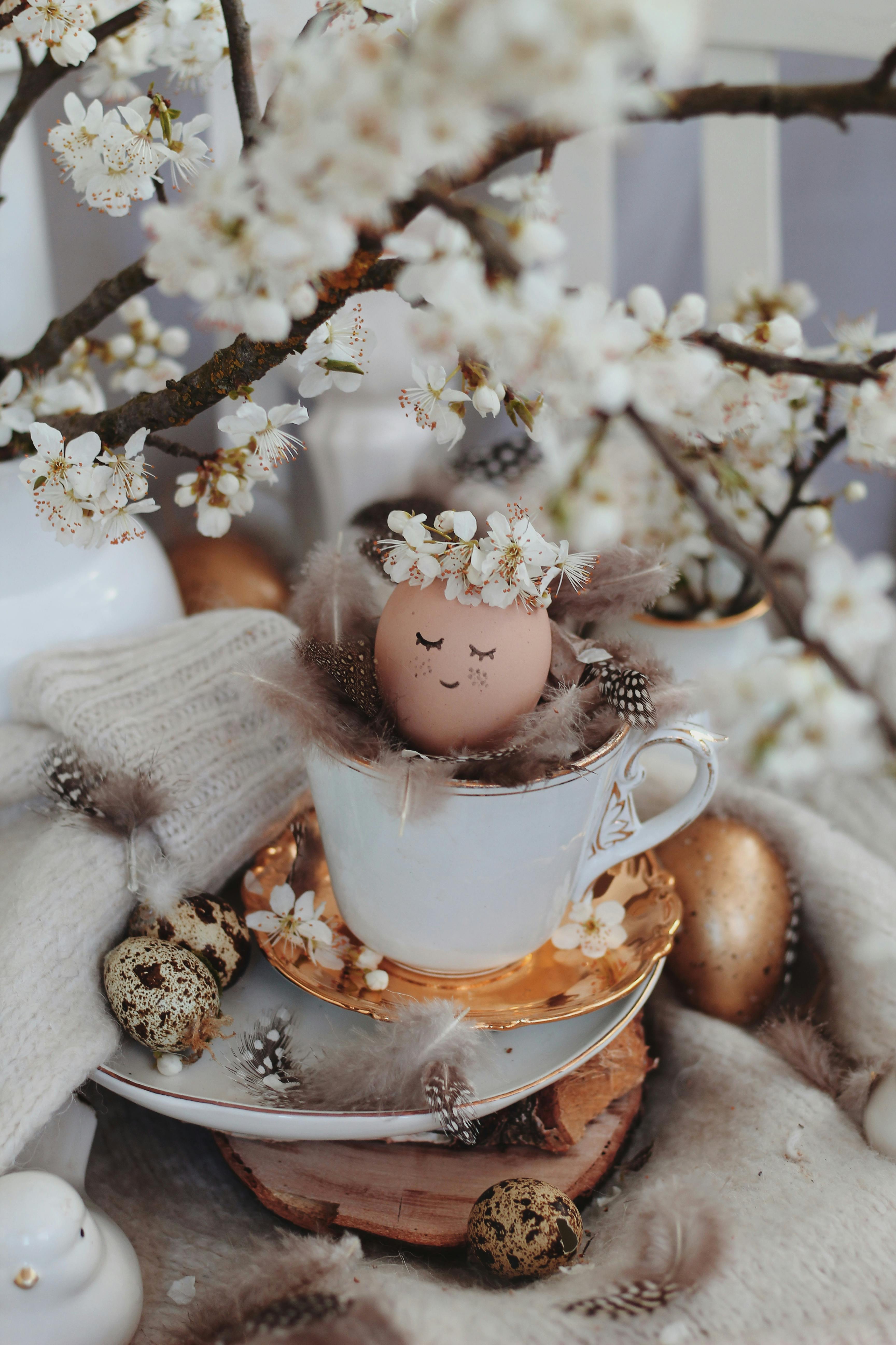 A charming Easter scene with a painted egg in a teacup surrounded by flowers and decorations.