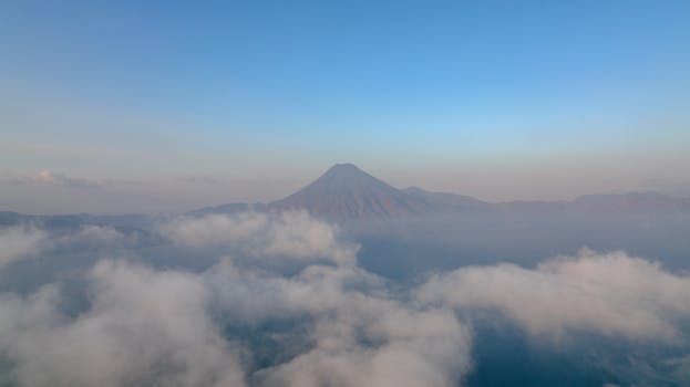 Stunning aerial view of a volcano surrounded by clouds against a clear blue sky.