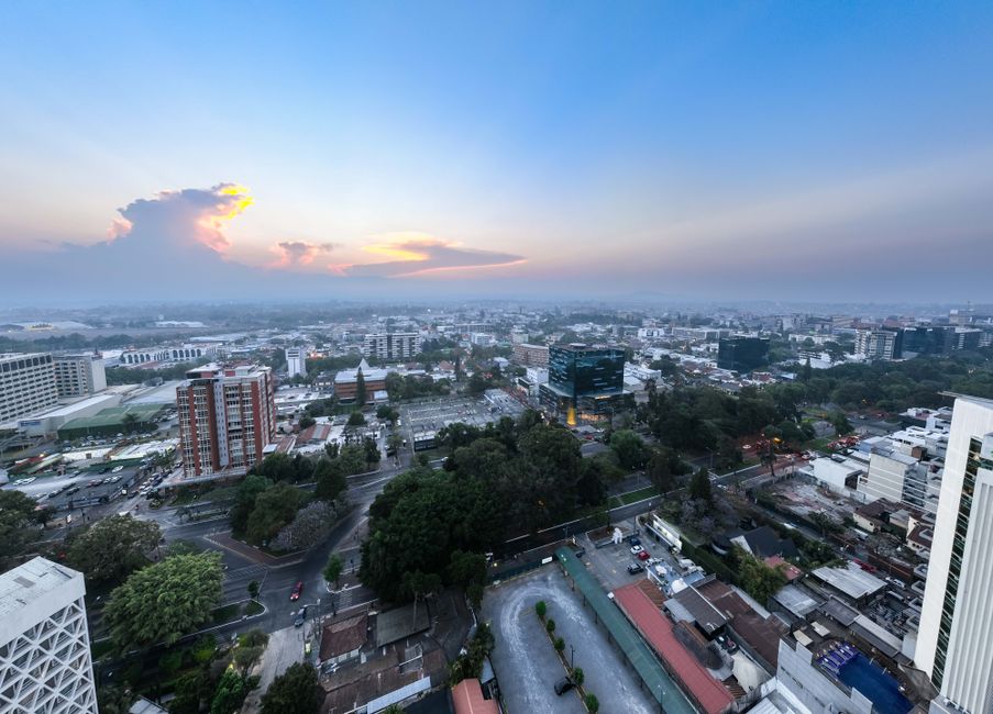 Panoramic aerial view of Guatemala City during sunset, showcasing urban landscape and skyline.