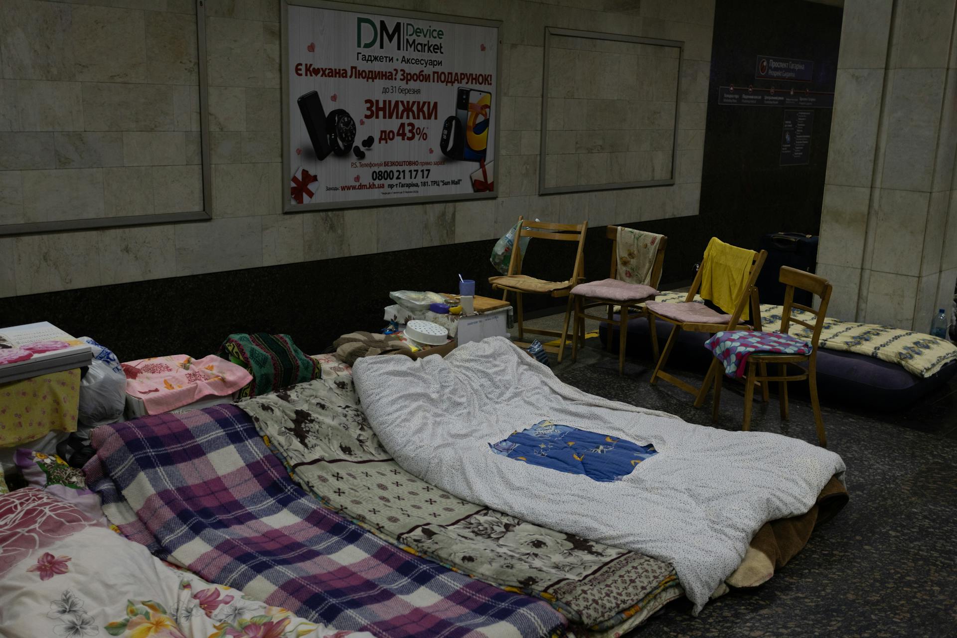 Makeshift sleeping area with chairs and bedding in an indoor underground setting, offering a glimpse into temporary housing arrangements.