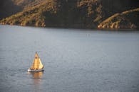 日落时分，一艘帆船滑行在宁静的湖面上，山丘郁郁葱葱