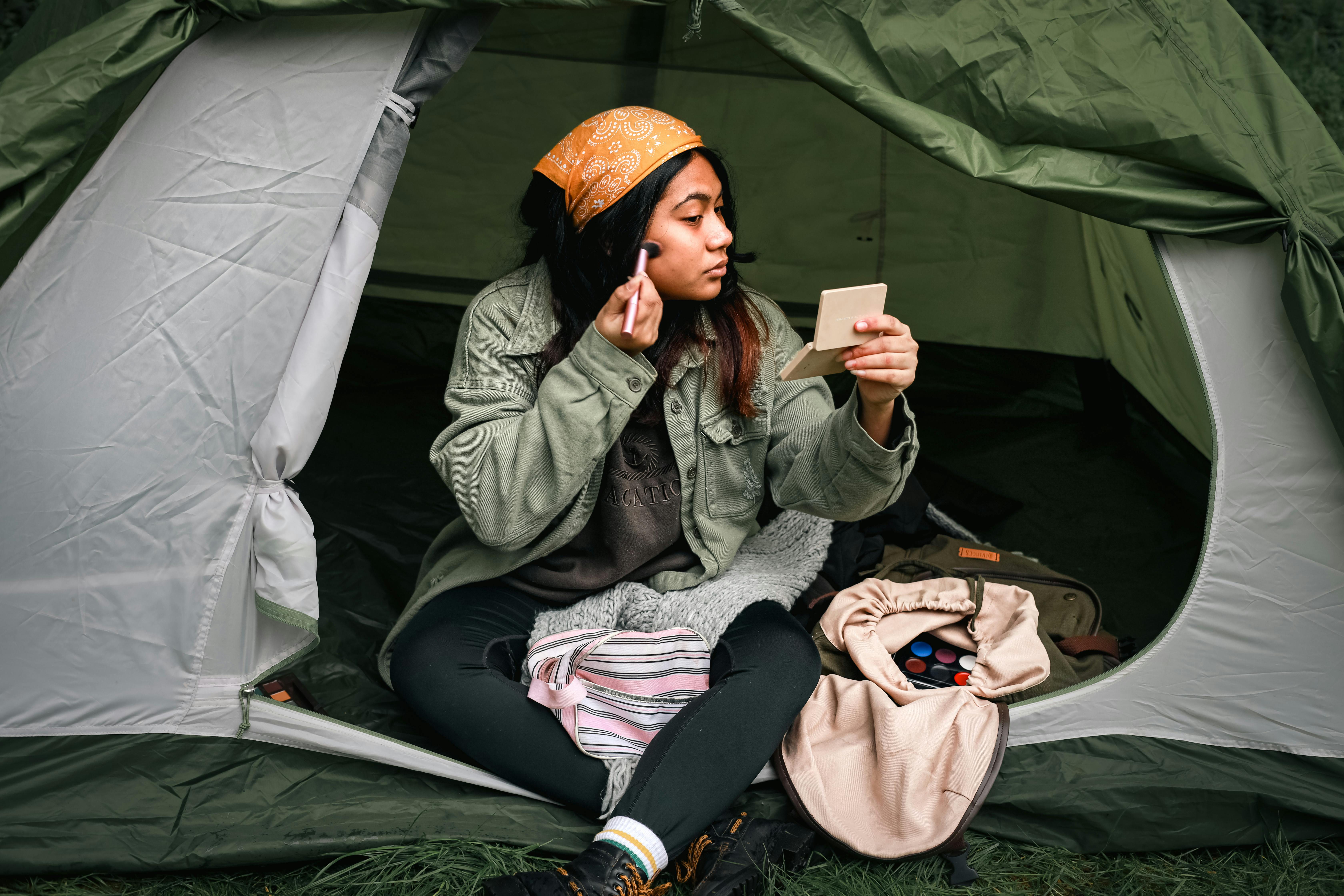 Young woman applying makeup while sitting in a tent, enjoying an outdoor camping trip.