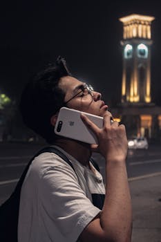A man making a phone call near a historic tower in Tashkent at night, showcasing urban life.