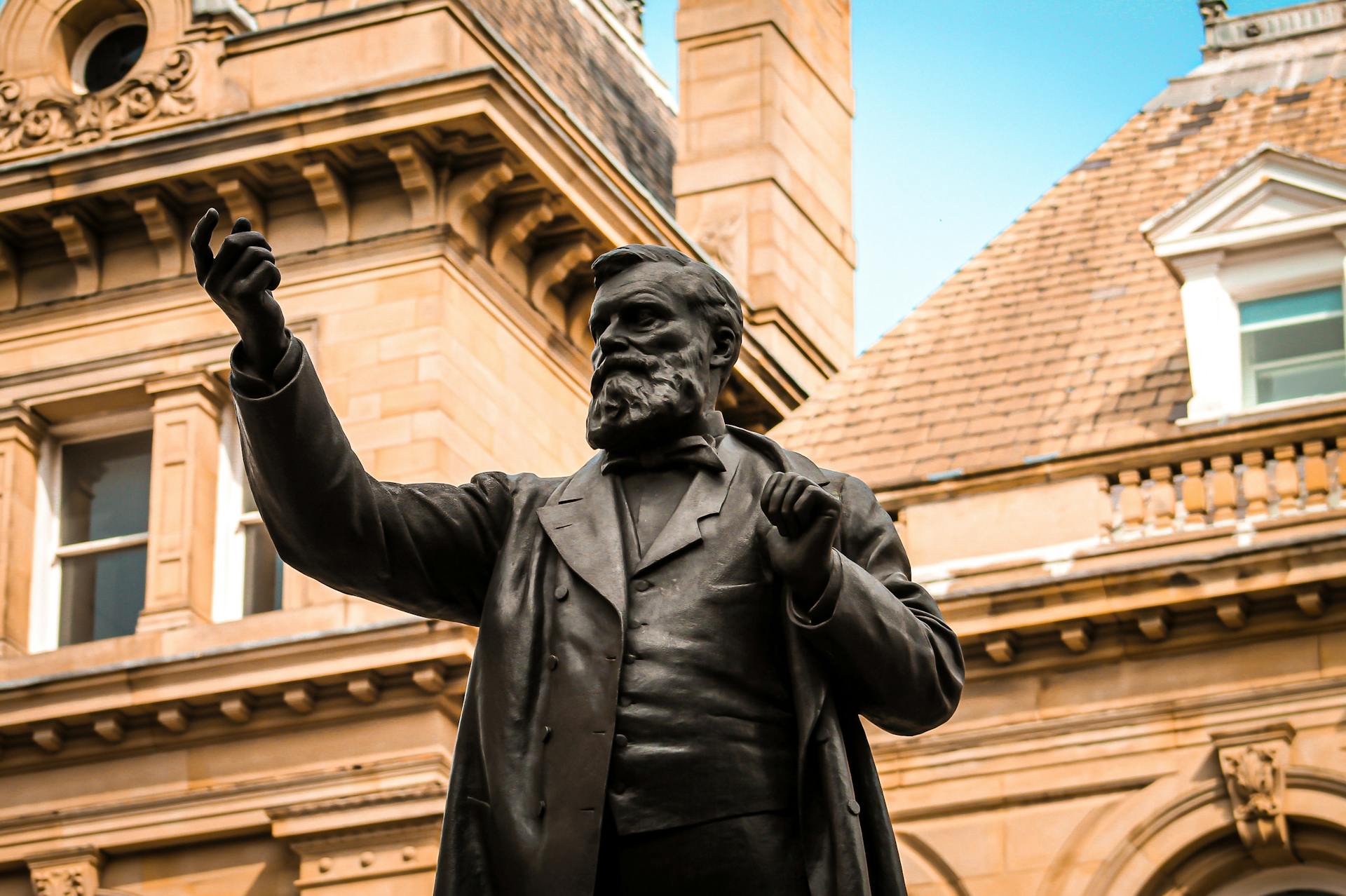 Bronze statue of W.E. Forster in front of historic architecture in Bradford, England.