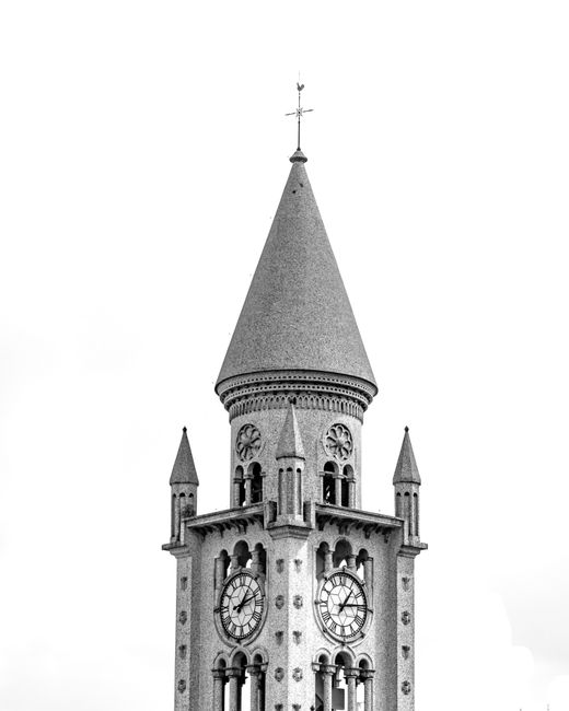 Striking black and white image of an ornate clock tower with a conical roof.