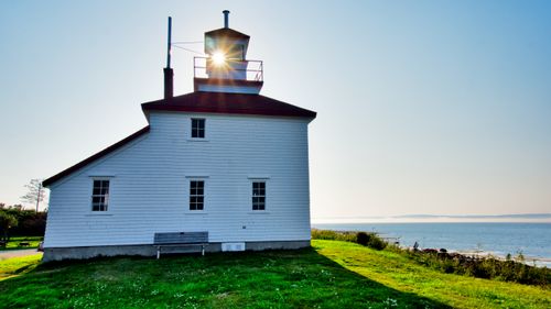 Free White lighthouse with ocean backdrop under a bright blue sky, perfect serene scene. Stock Photo