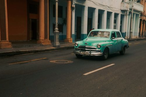 Free A classic car drives through a charming, colorful street, evoking nostalgia. Stock Photo