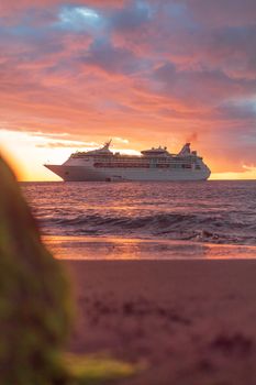 A majestic cruise ship sails through the Caribbean Sea at sunset, creating a stunning view from Grenada's shore.