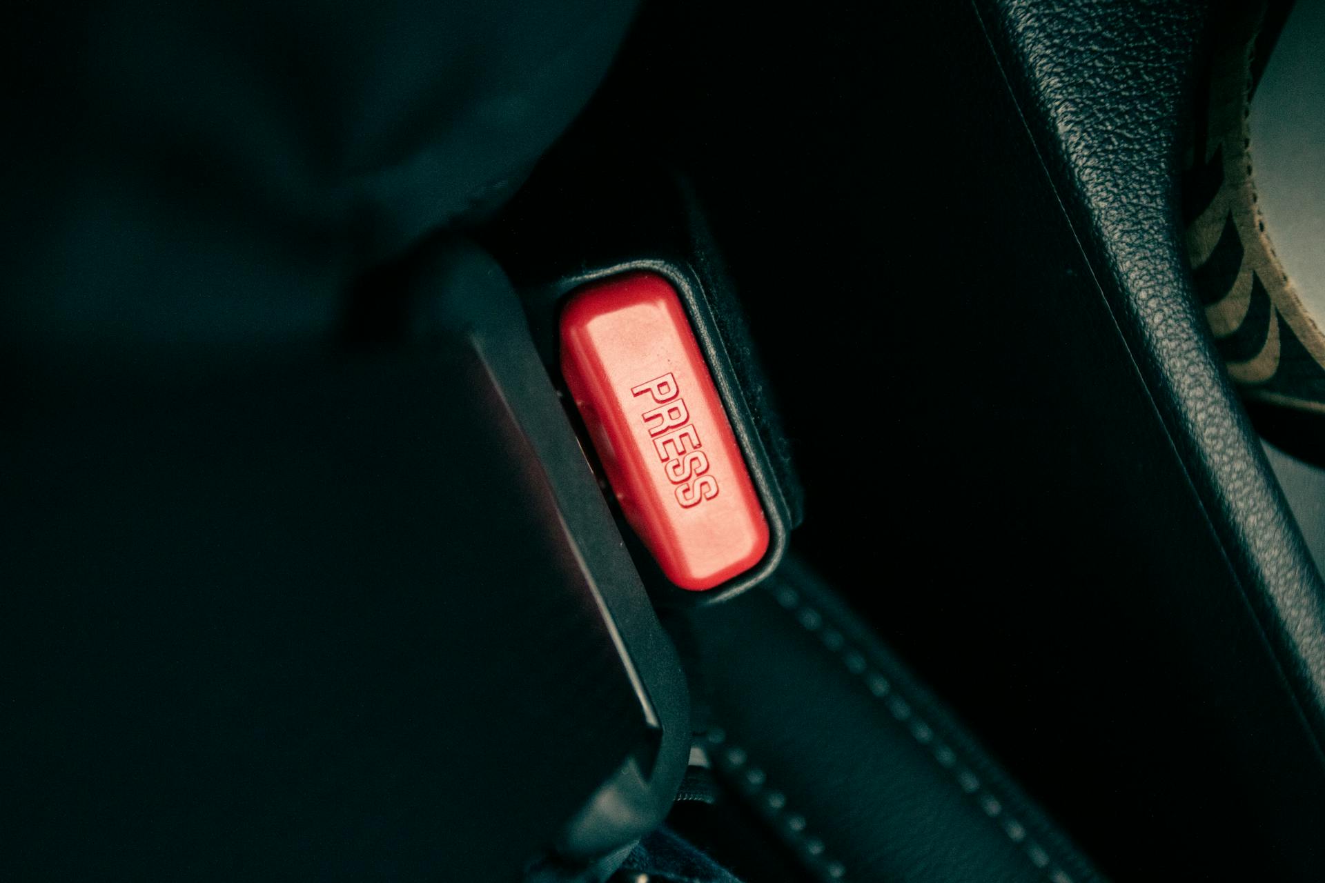 Detailed view of a car seatbelt buckle with a red press button.