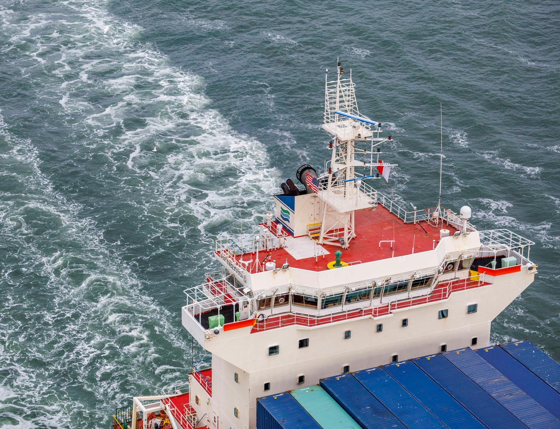Aerial shot of a cargo ship navigating through ocean waves with visible container deck.