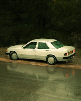 Classic white car parked on a wet road in Algeria, reflecting a vintage aesthetic.