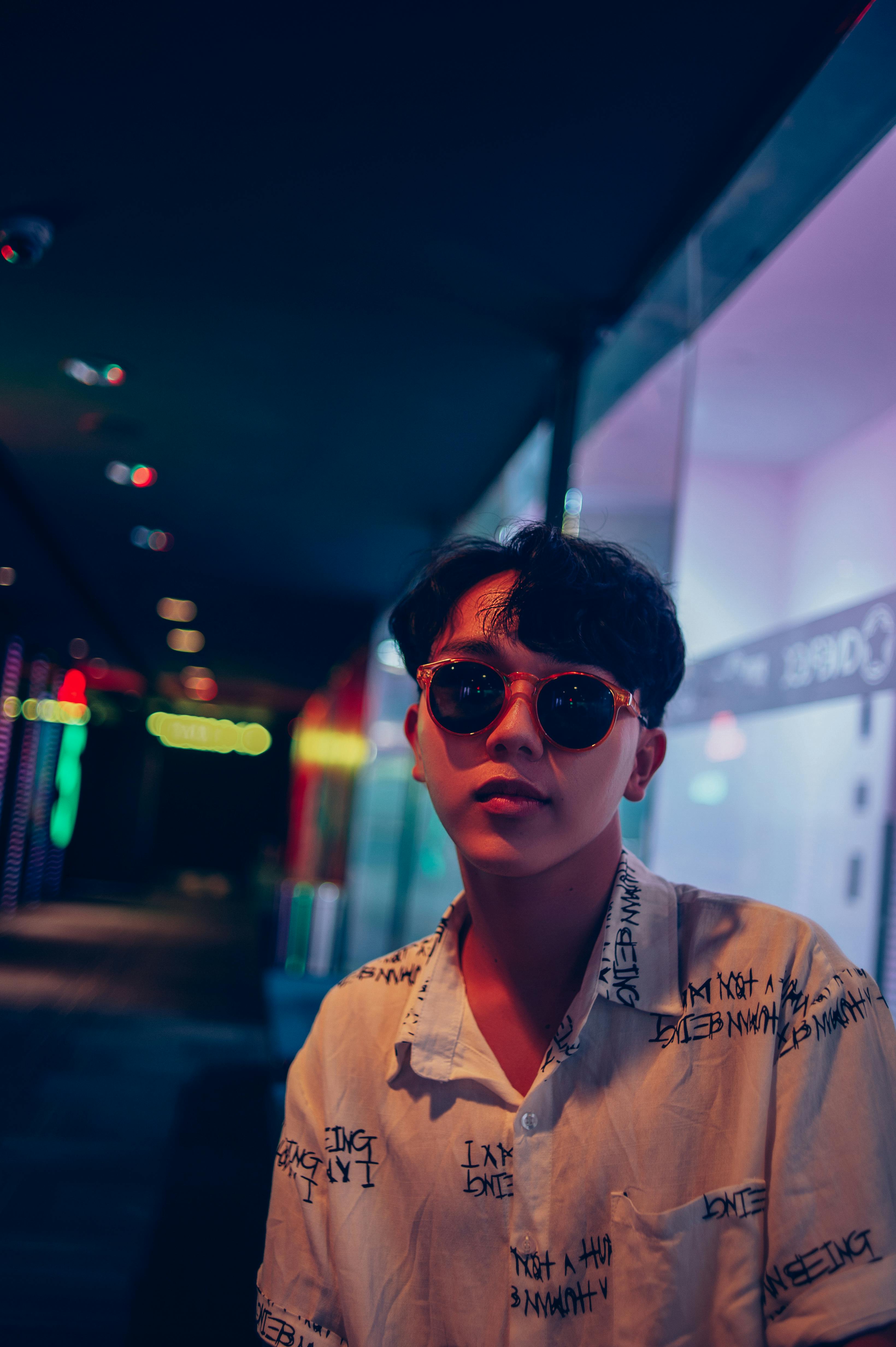 Portrait of a young man in sunglasses and casual wear at night in Đắk Ya, reflecting urban style.