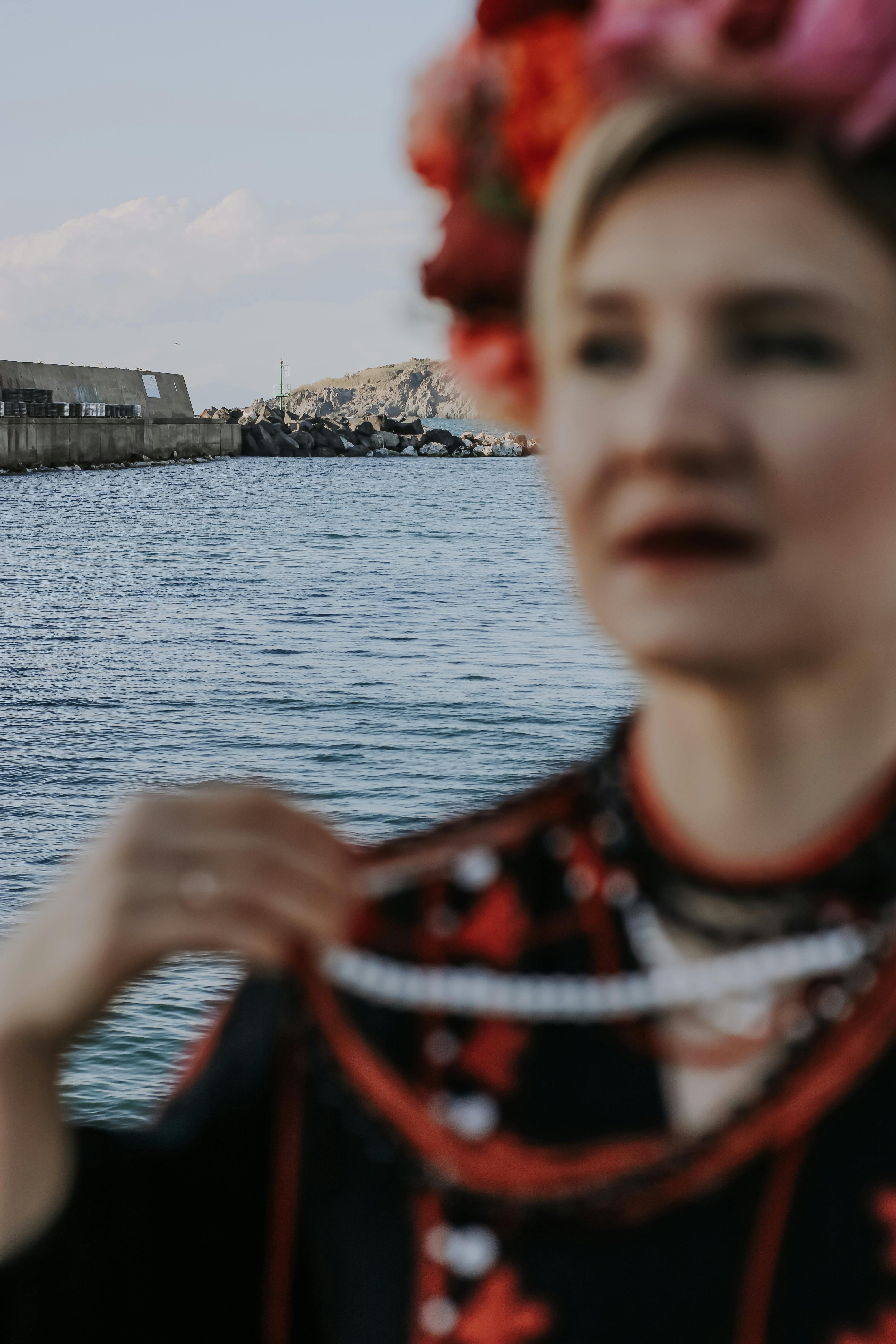 Blurred woman with vibrant headdress and necklace by the sea, conveying a dramatic mood.