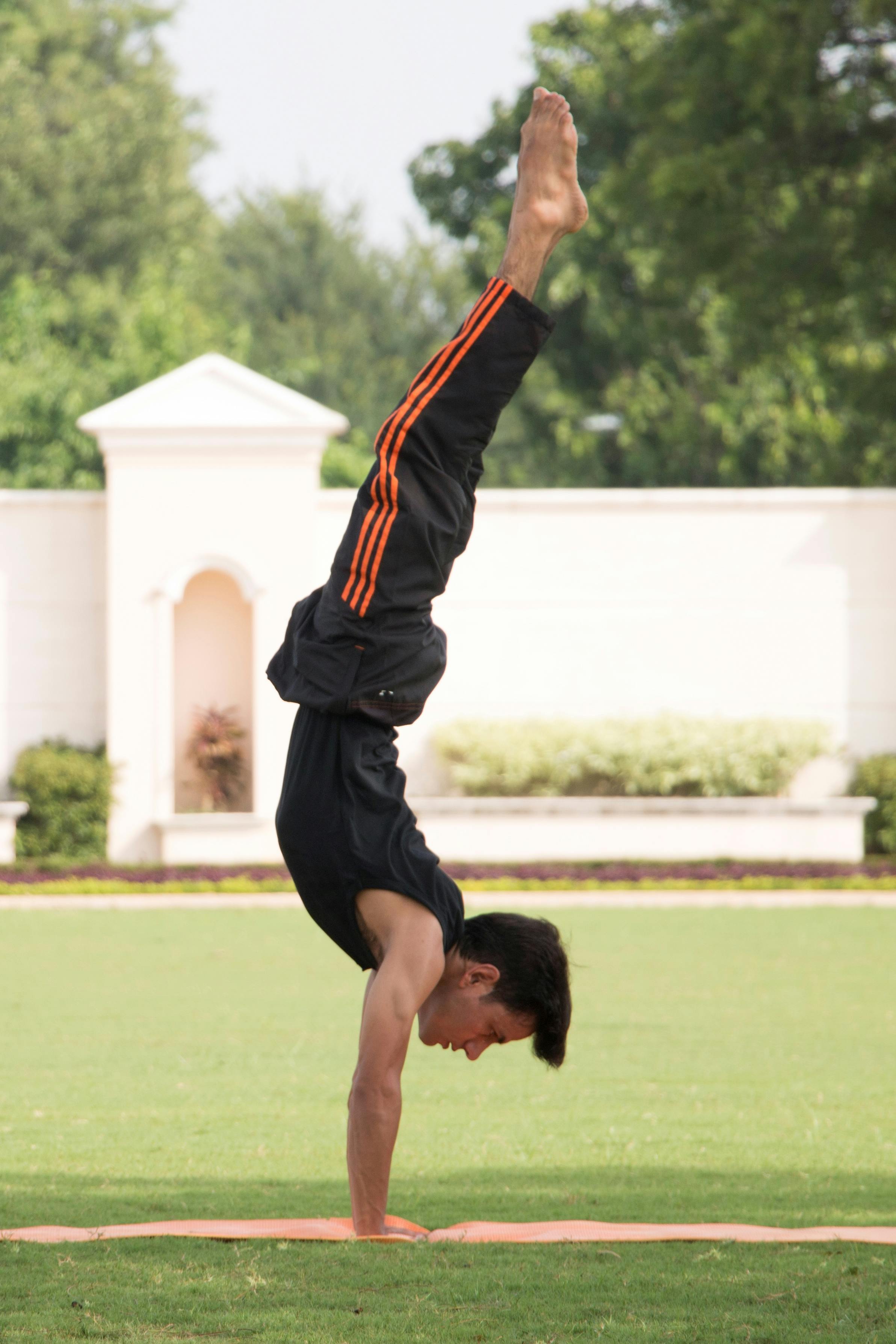 Adult man practicing handstand outdoors on a sunny day, showcasing strength and balance.