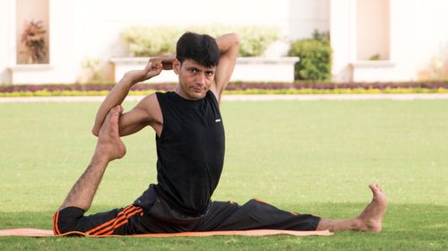 Free Man performing a yoga pose outdoors on grass, showcasing flexibility and concentration. Stock Photo