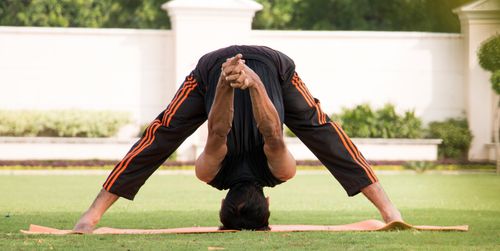 Free Man performing a yoga headstand on grass in a peaceful outdoor setting, showcasing flexibility and balance. Stock Photo