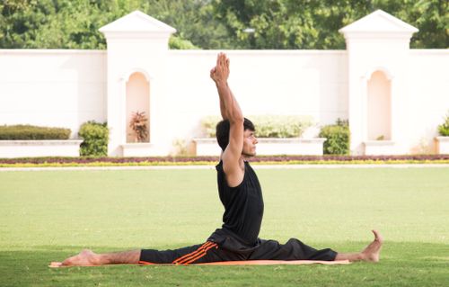 Free Man performing a yoga stretch on grass in an outdoor park setting, demonstrating flexibility and fitness. Stock Photo
