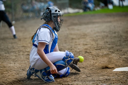 A female catcher in full gear catching a softball during an outdoor game.