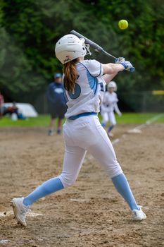 Female softball player swinging a bat during a game on an outdoor field, showcasing athletic motion.