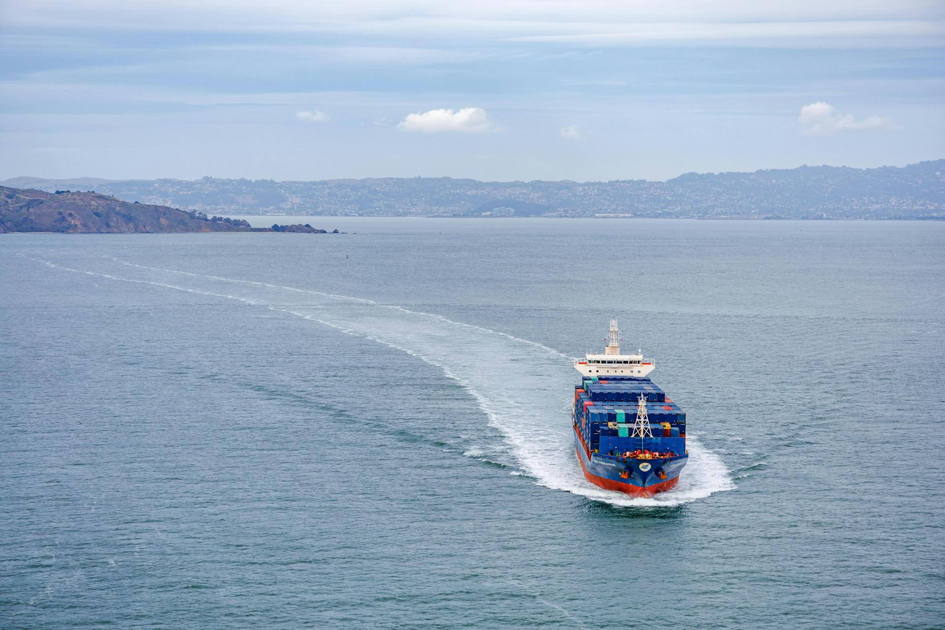 A cargo ship filled with containers travels across calm ocean waters on a clear day.