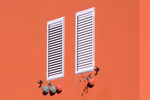 Minimalist image featuring orange wall with white shutters and hanging clay pots.