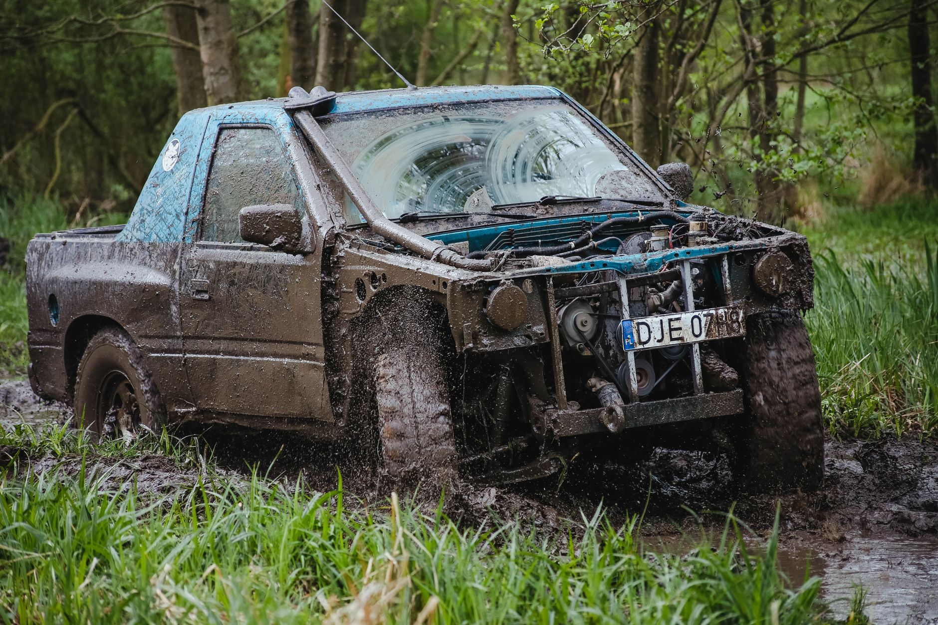 Mud-covered pickup truck driving through a deep forest mud pit, showing why recovery gear matters for hunting season off-road driving