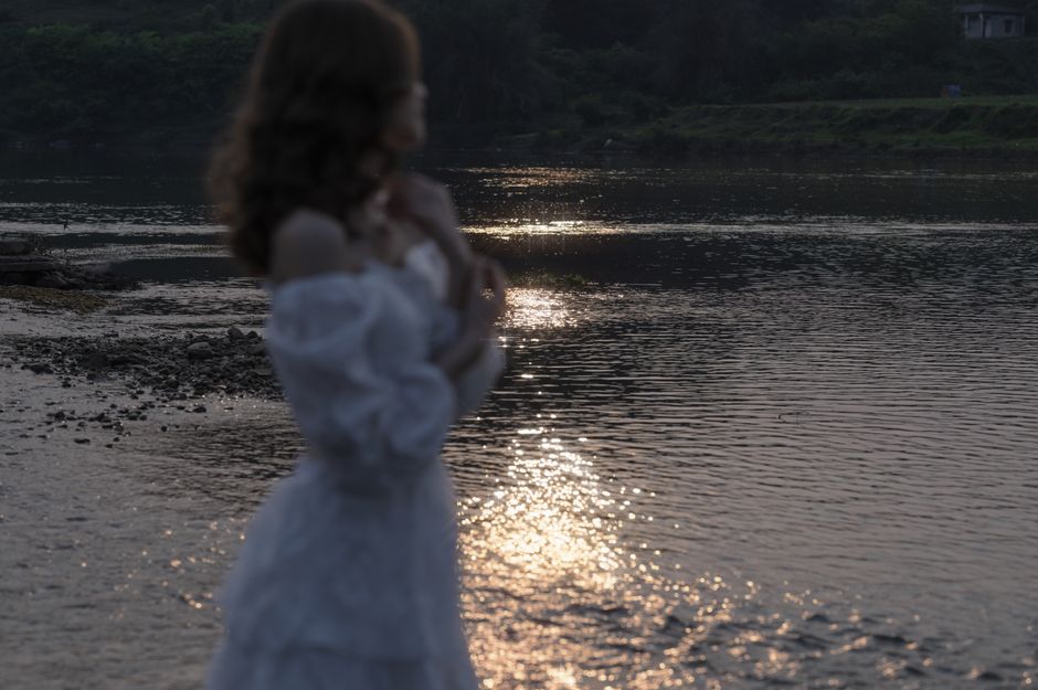 A woman in a white dress stands by a serene river reflecting the sunset in Lạng Sơn, Vietnam.