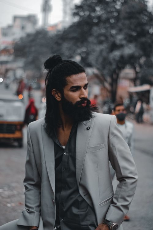 Free Bearded man with long hair in a gray suit posing outdoors on a busy city street. Stock Photo