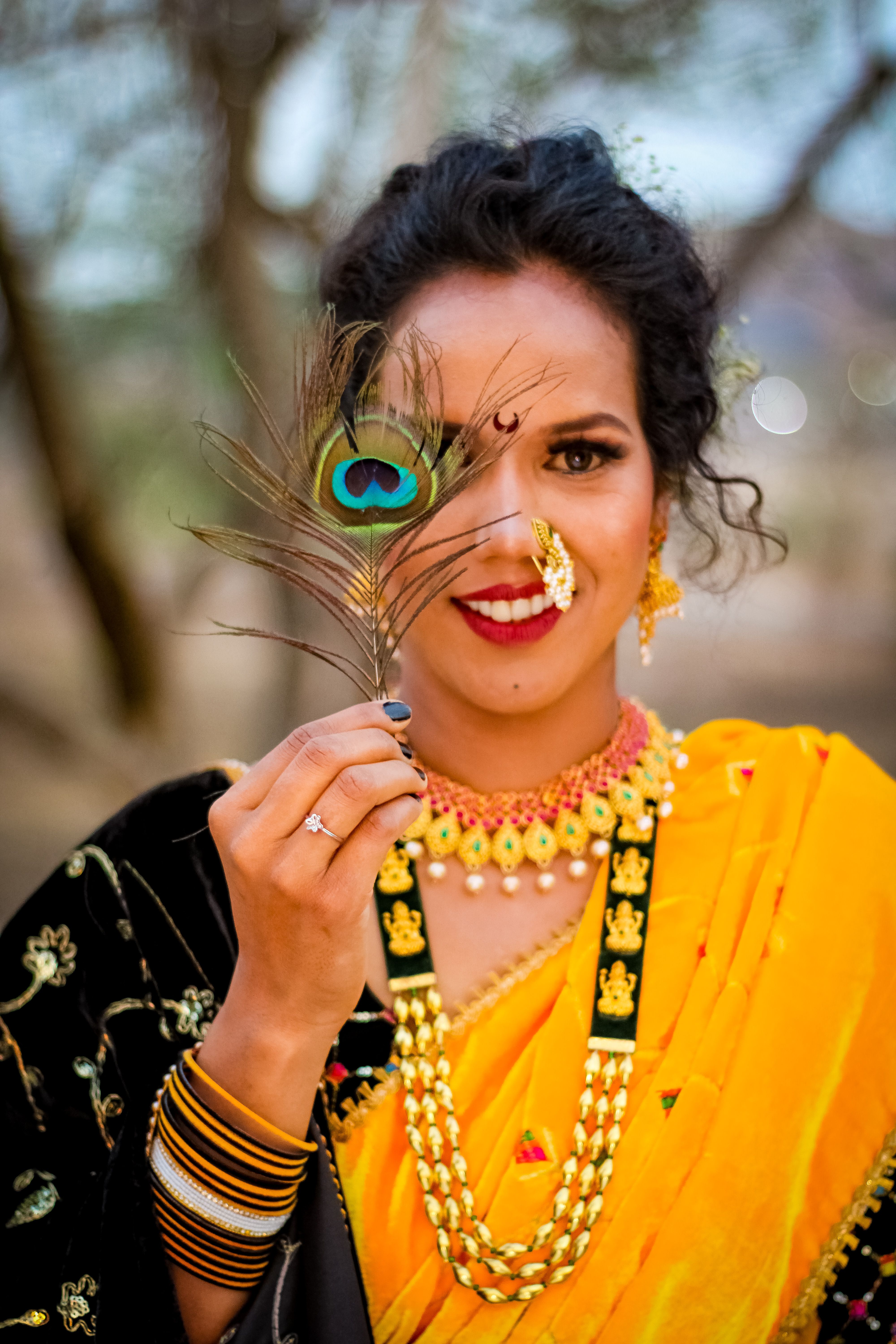 A beautifully dressed woman in traditional Indian clothing with vibrant jewelry holding a peacock feather.