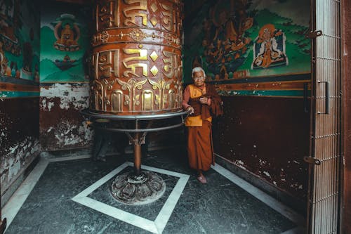 Elderly Monk standing beside a Prayer Wheel