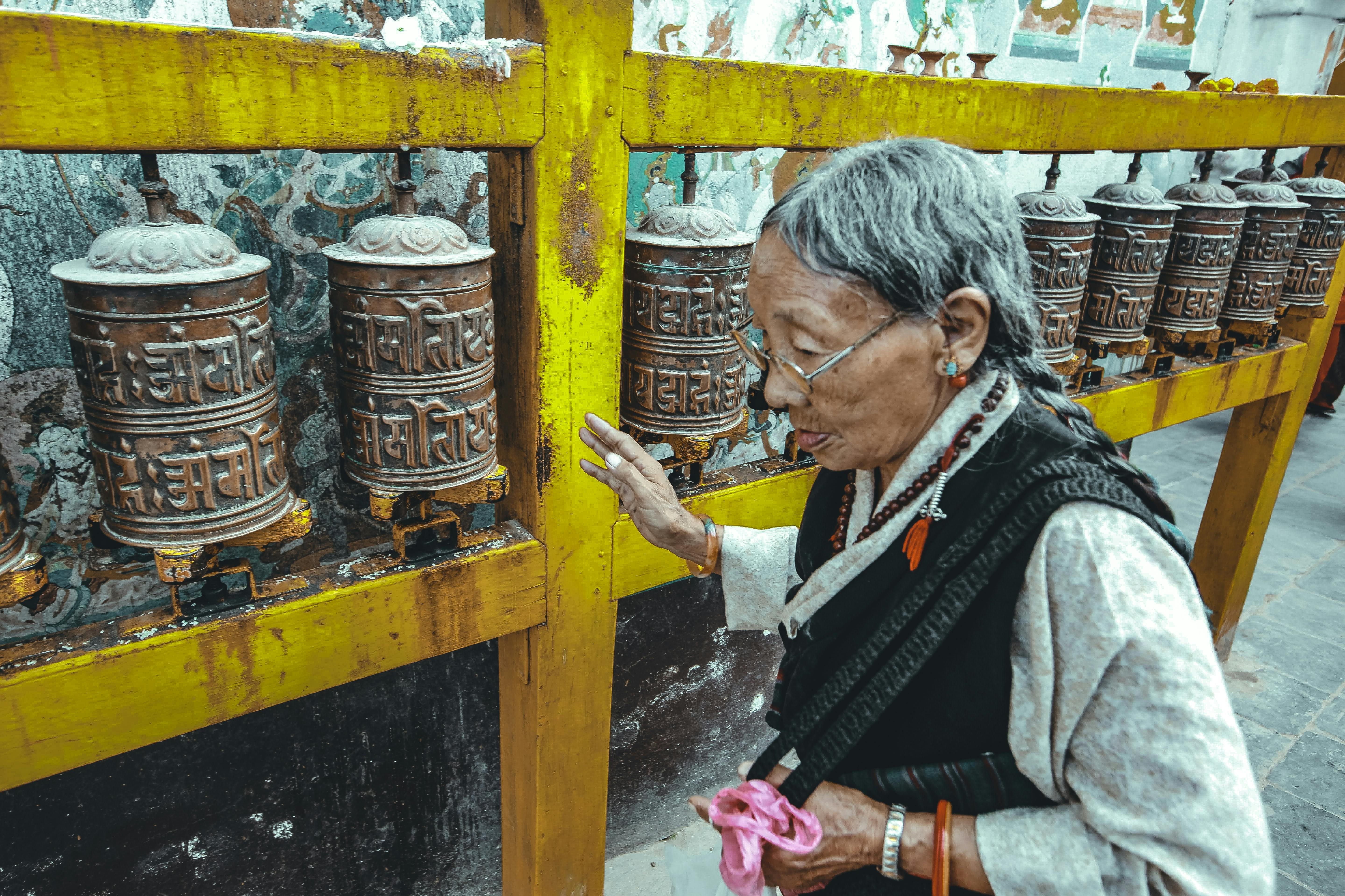 Senior woman interacting with traditional prayer wheels in an ornate temple environment.