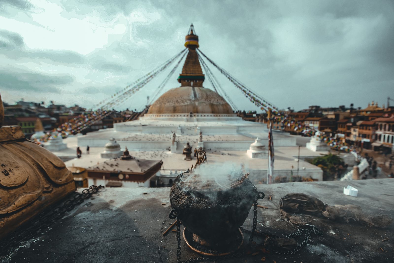 Incense smoke rising from a burner on a rooftop facing Boudhanath stupa in Kathmandu, prayer flags strung from its spire