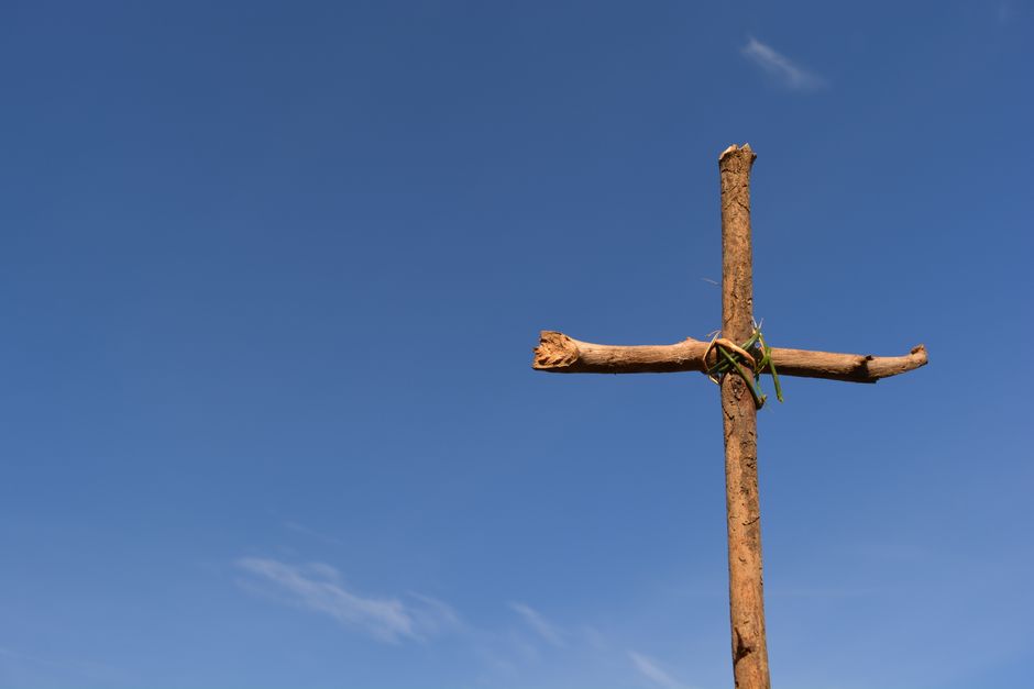 A rustic wooden cross stands against a clear blue sky, symbolizing faith and spirituality.