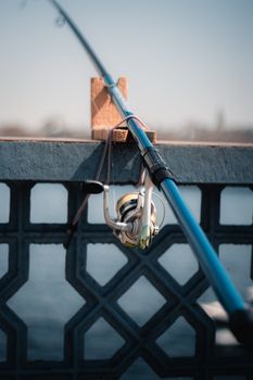 A fishing rod resting on a decorative concrete railing by the water on a clear day.