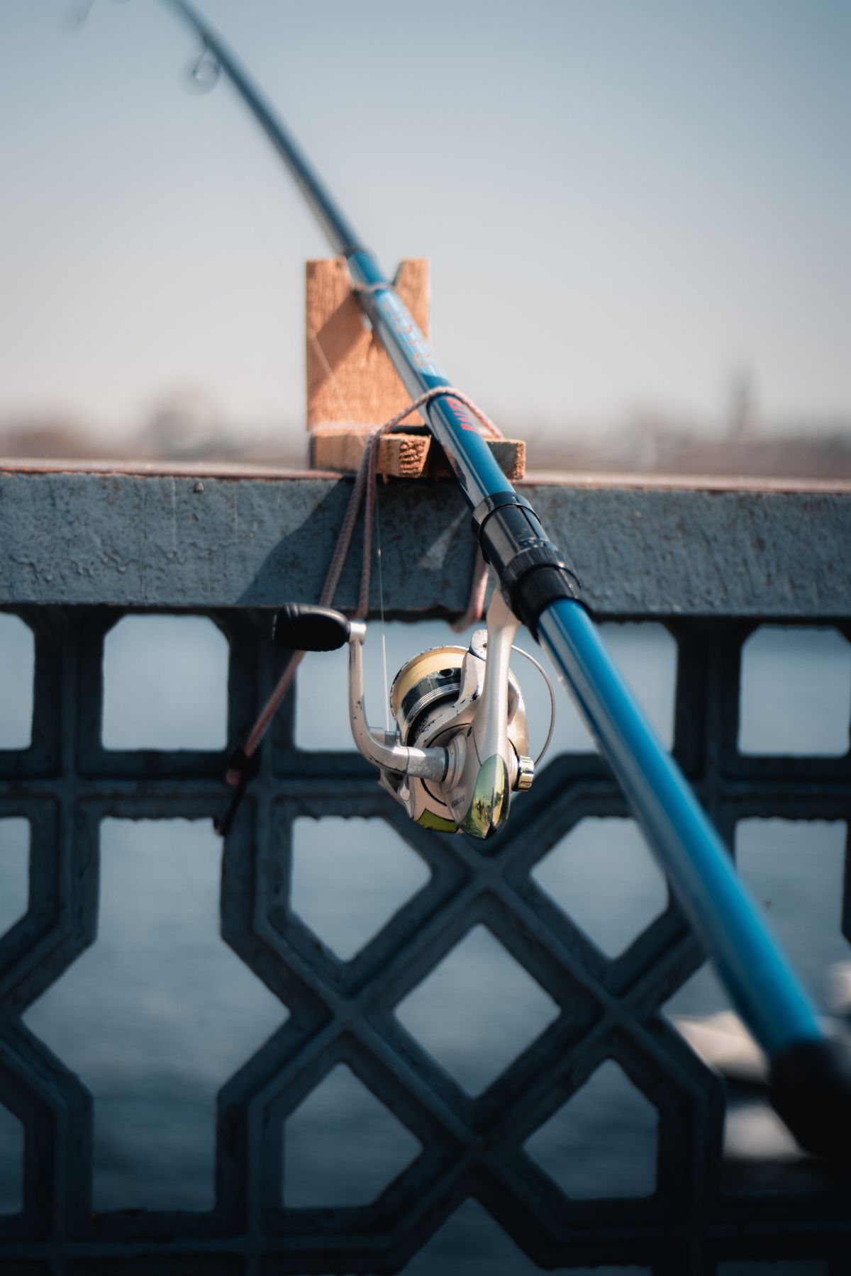 A fishing rod resting on a railing by the water on a clear day