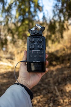 A hand holding a Zoom audio recorder in a wooded area, ideal for field recording.