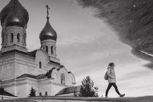 Black and White Photo of a Woman Walking near a Church