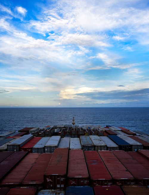 Free Aerial view of a cargo ship transporting containers over a calm ocean under a blue sky. Stock Photo
