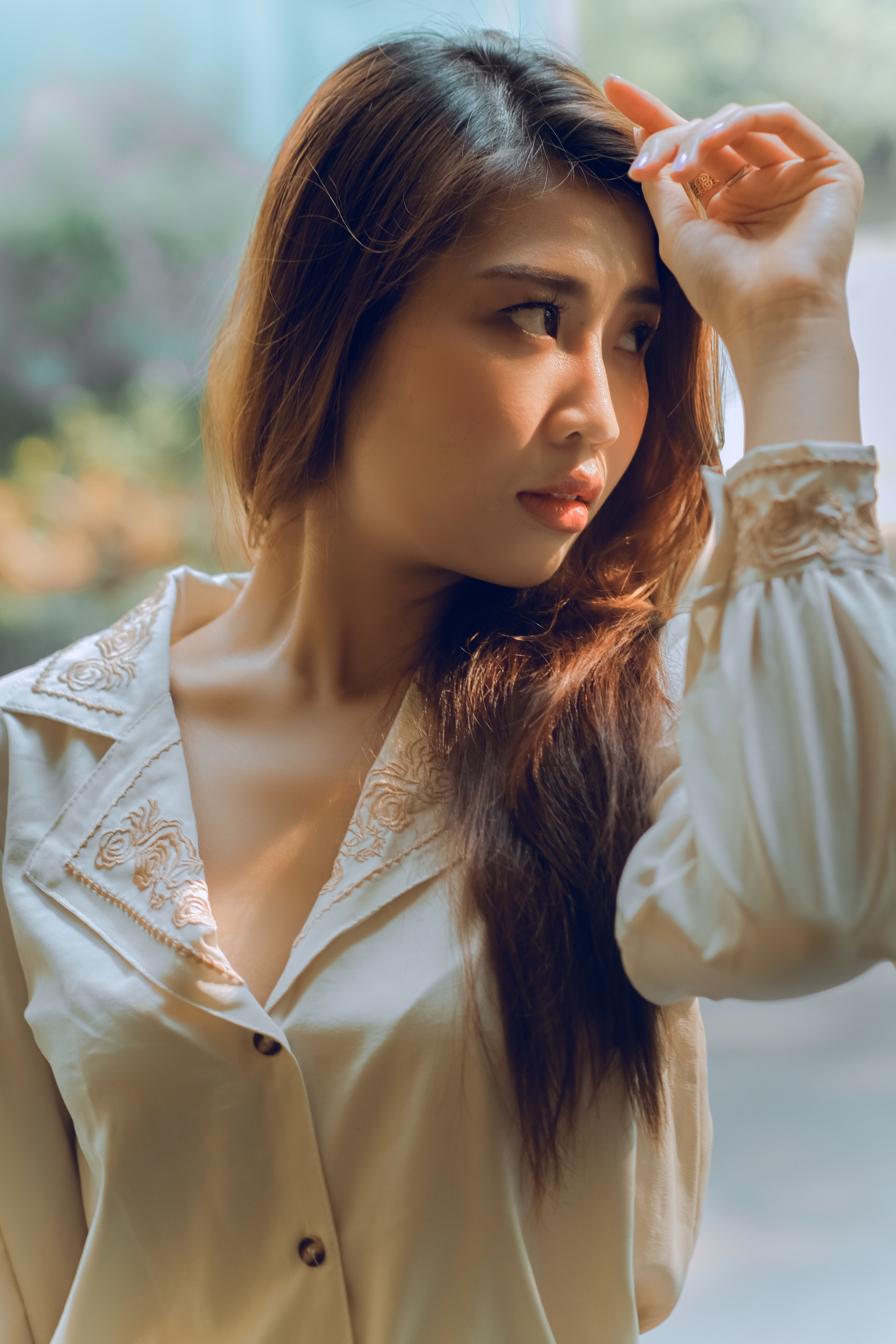 A beautiful woman posing thoughtfully in a soft-lit setting with a white blouse.