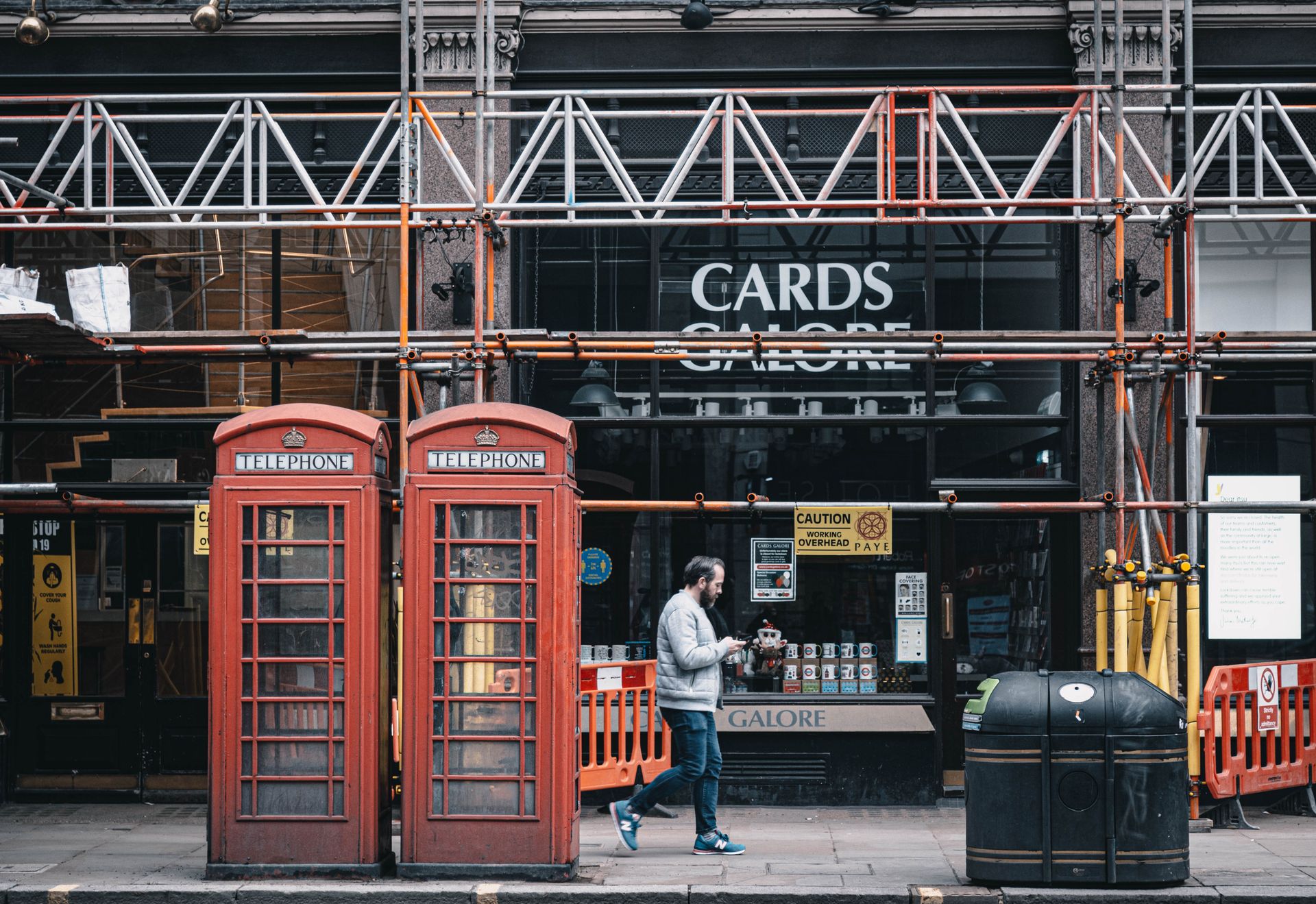 Man walking past iconic red telephone booths in London, with street construction.