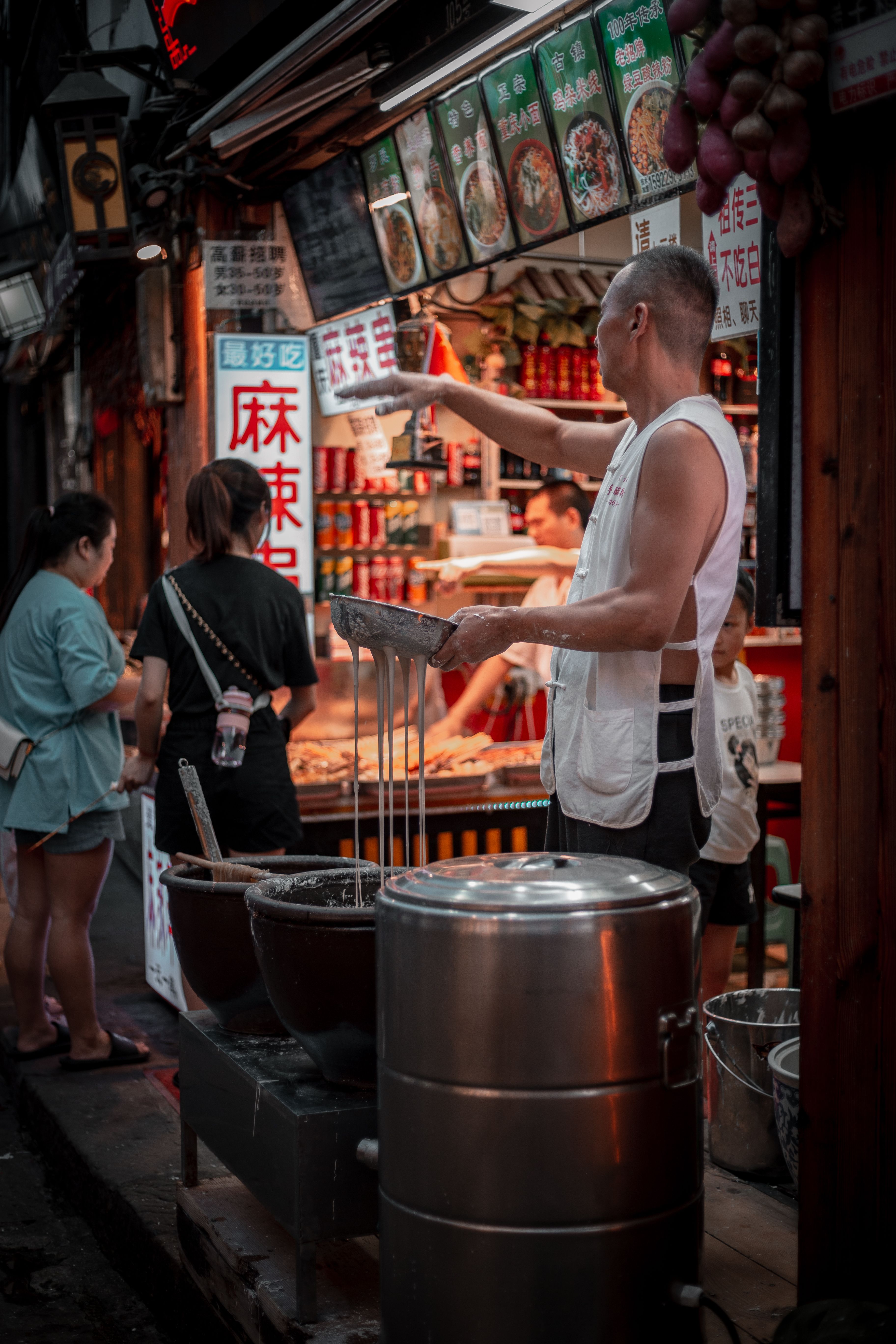 Street vendor in Chongqing, China, preparing traditional dishes in a bustling market setting.