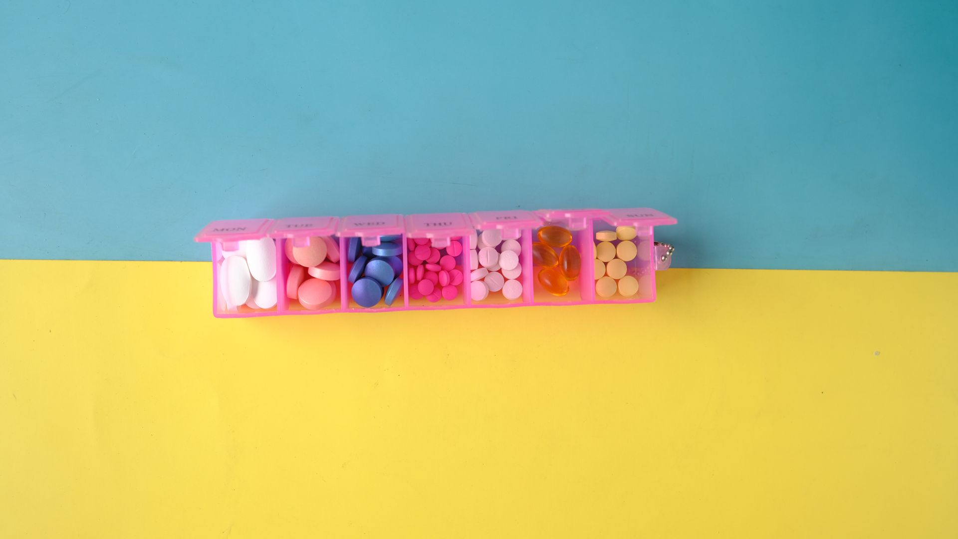 Modafinil Half Tablet Dosing Guide: Maximizing Benefits A vibrant photo of assorted pills in a pink organizer on a blue and yellow background, ideal for health topics — modafinil half tablet dosing guide