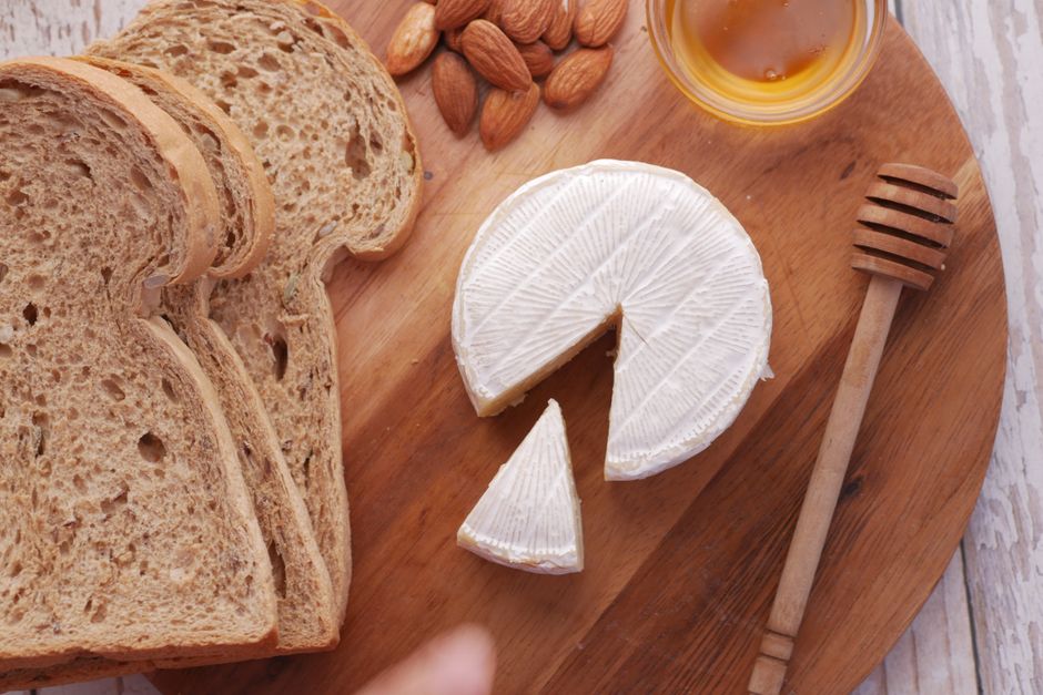 Rustic breakfast platter with brie cheese, almonds, and honey on a wooden board.