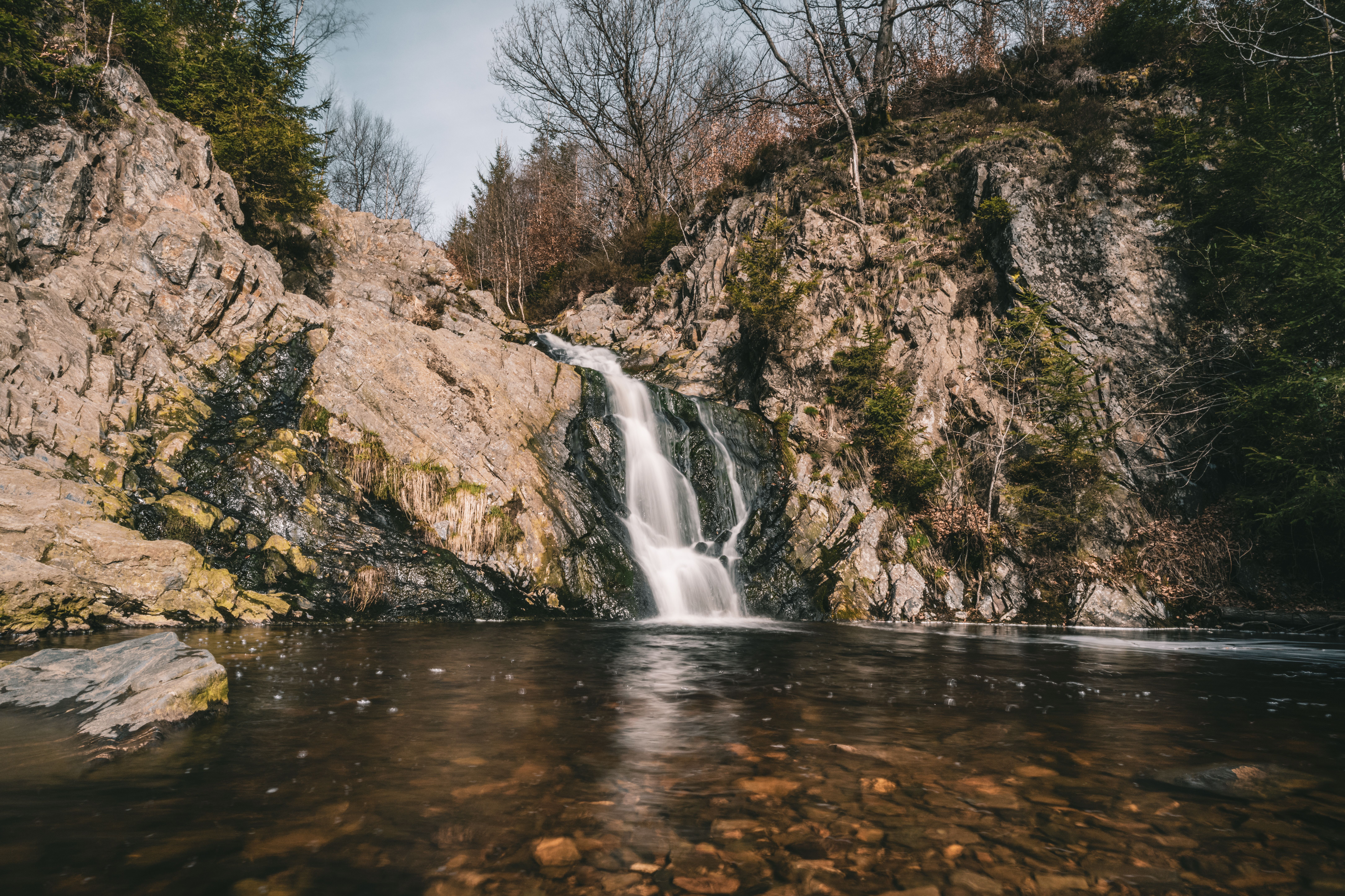 A tranquil waterfall flows over rocky cliffs surrounded by trees, showcasing nature's beauty.