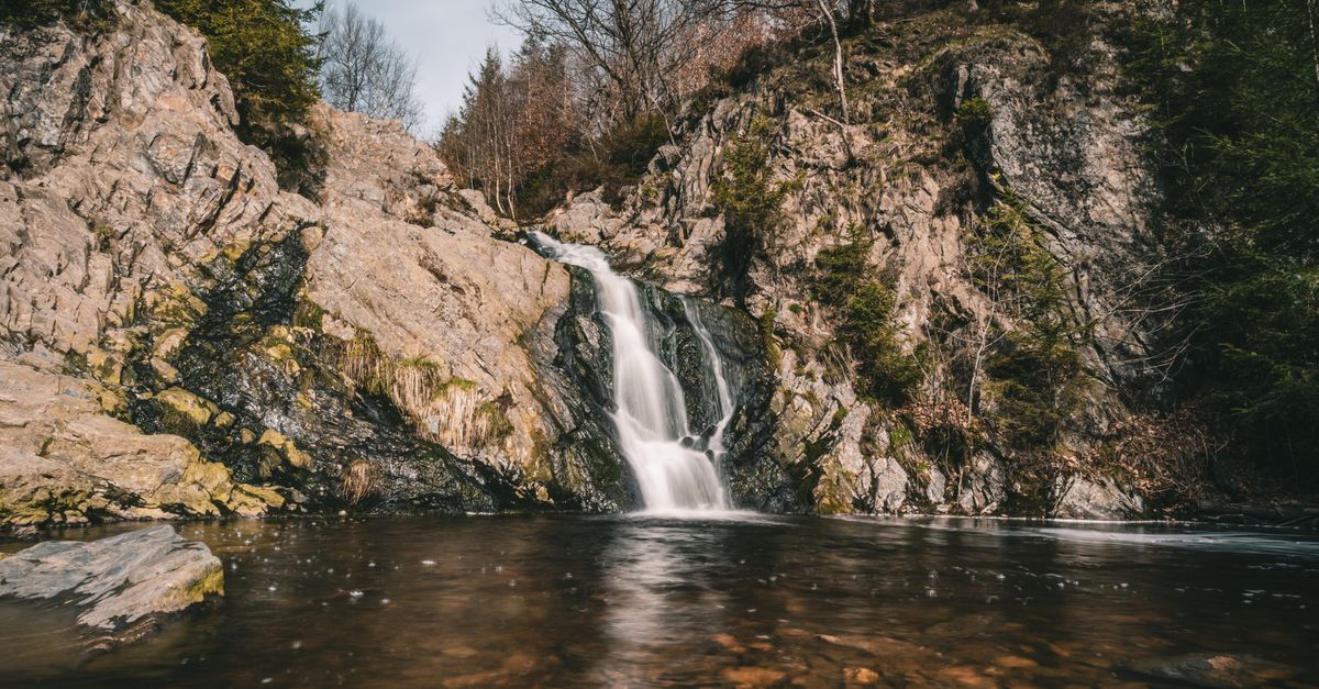 A tranquil waterfall flows over rocky cliffs surrounded by trees, showcasing nature's beauty.