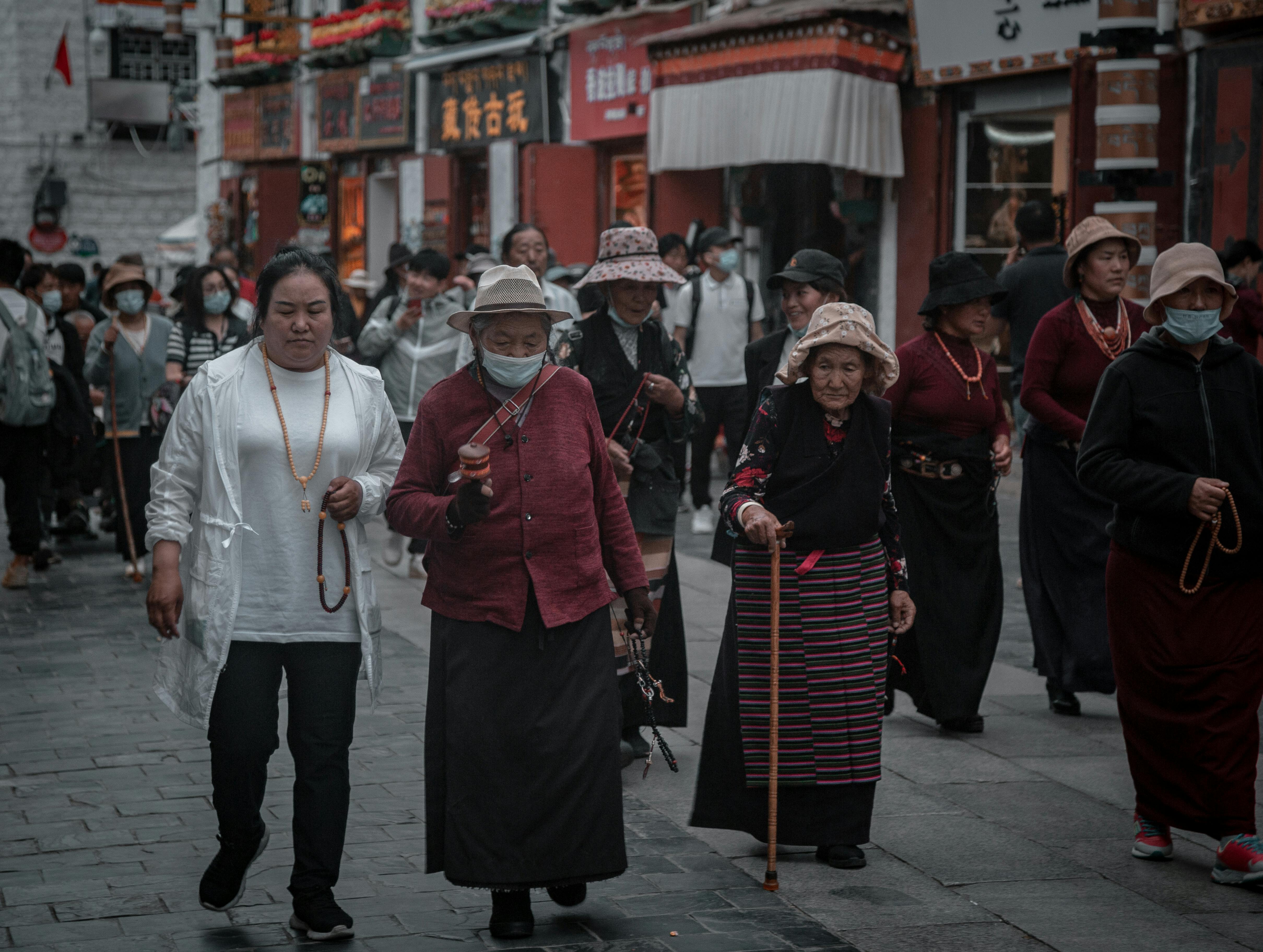 A group walks through a bustling street in Tibet, showcasing traditional attire and vibrant local culture.
